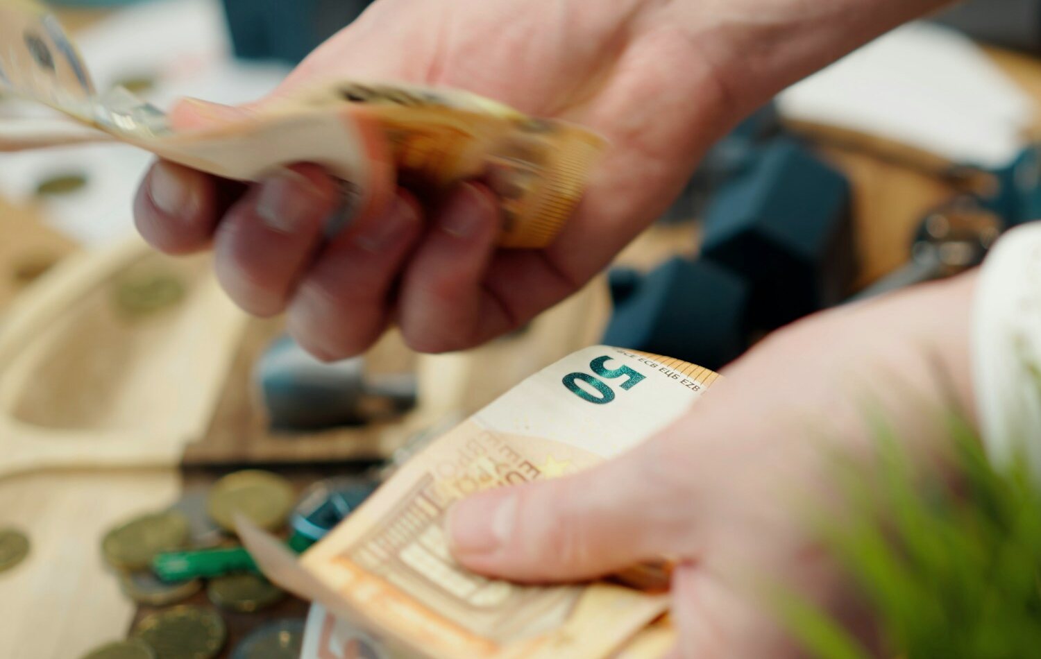 Hands counting euro banknotes above coins at a desk